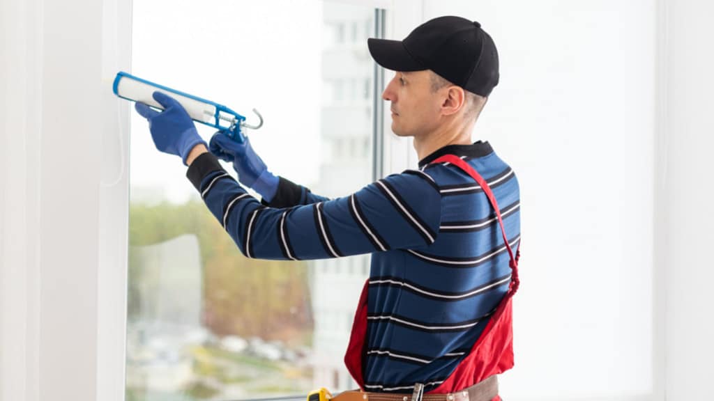 worker applying caulk to window frame for sealing gaps
