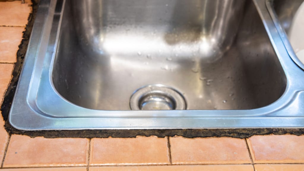 kitchen sink with cracked and moldy caulk around edges