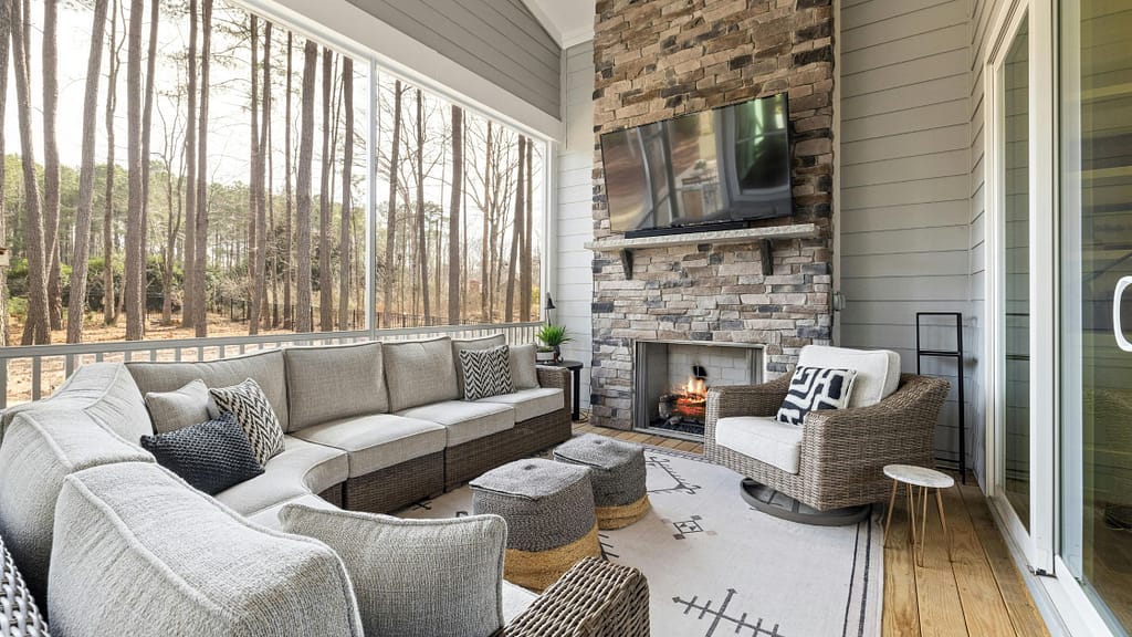 Large TV mounted high above stone fireplace on screened porch