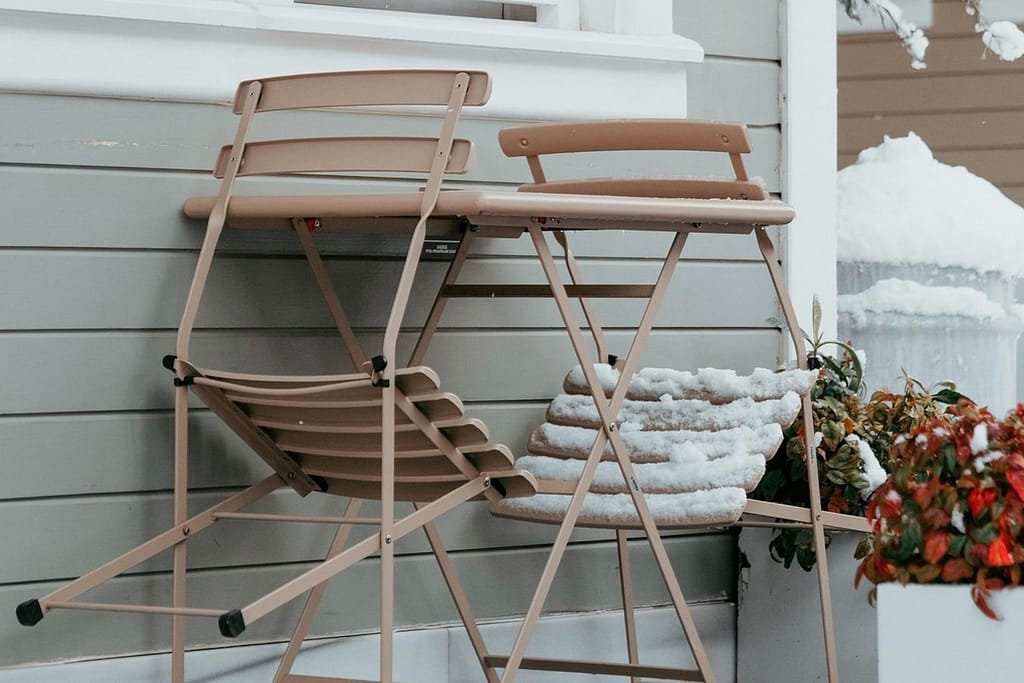 Outdoor chairs and table covered in snow beside a house