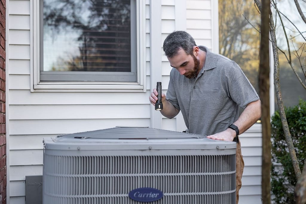 Homeowner inspecting an outdoor HVAC unit before winter