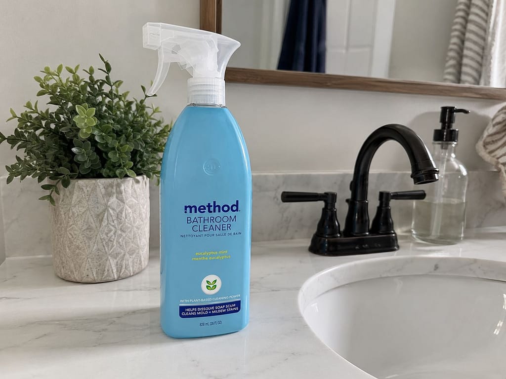 Method bathroom cleaner bottle on a bathroom counter beside a sink, plant and black faucet.
