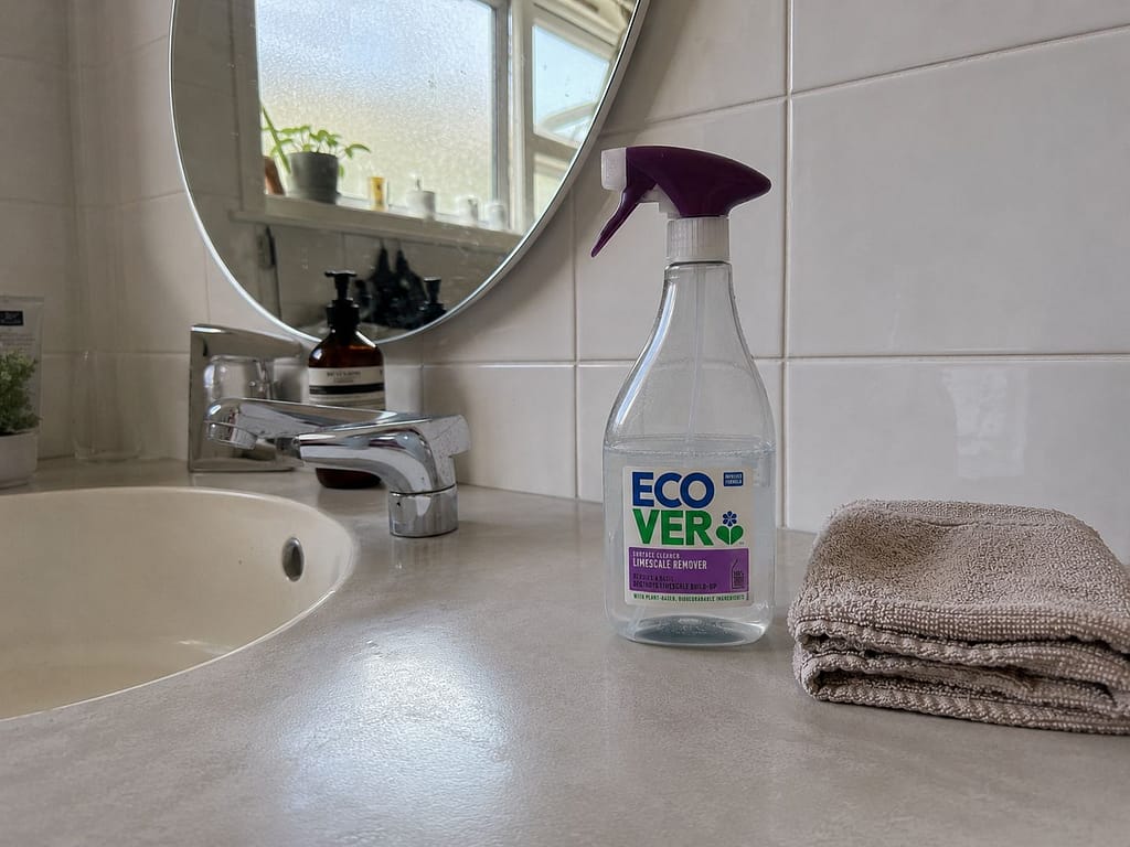 EcoVer limescale remover spray bottle on a bathroom counter beside folded towels and a sink.