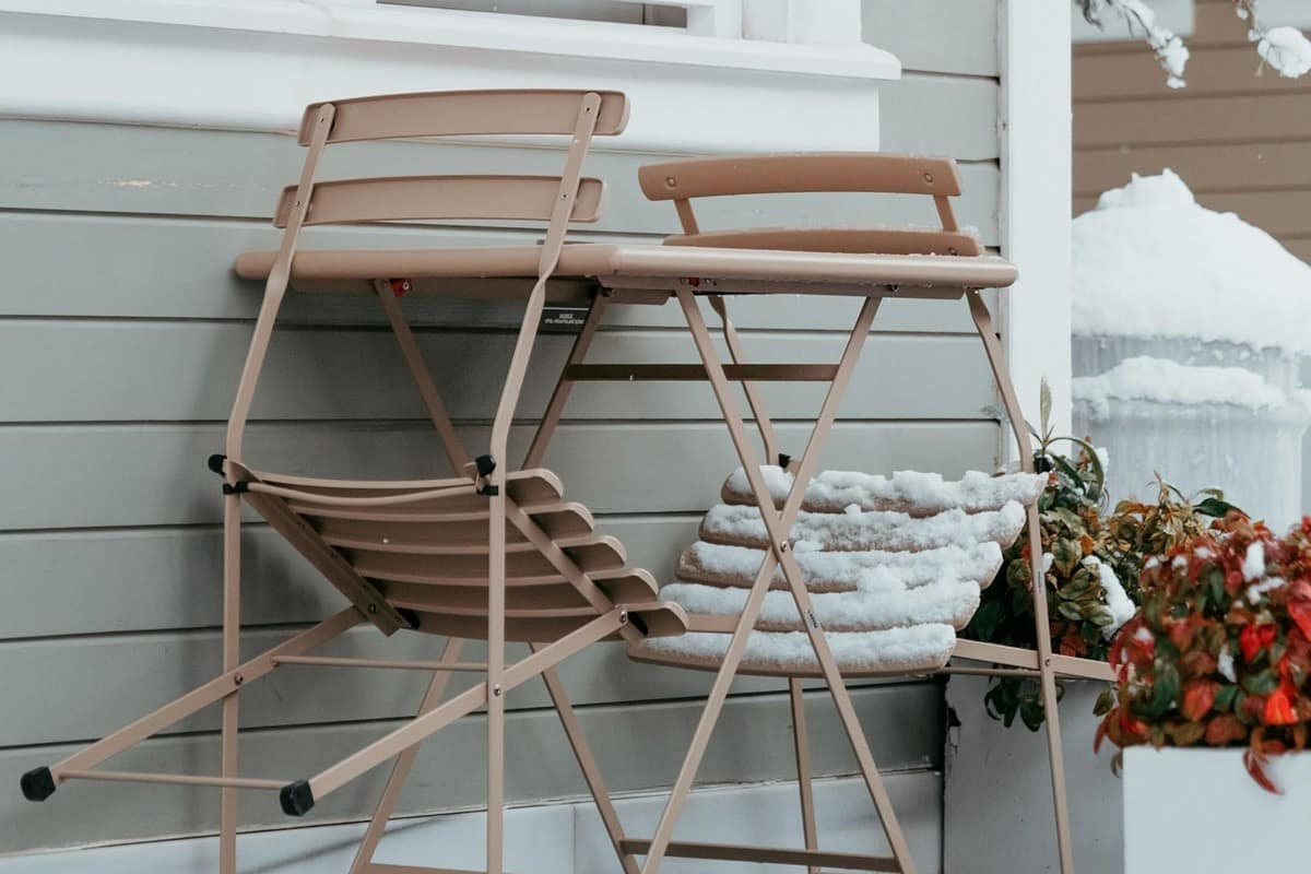 Outdoor chairs and table covered in snow beside a house