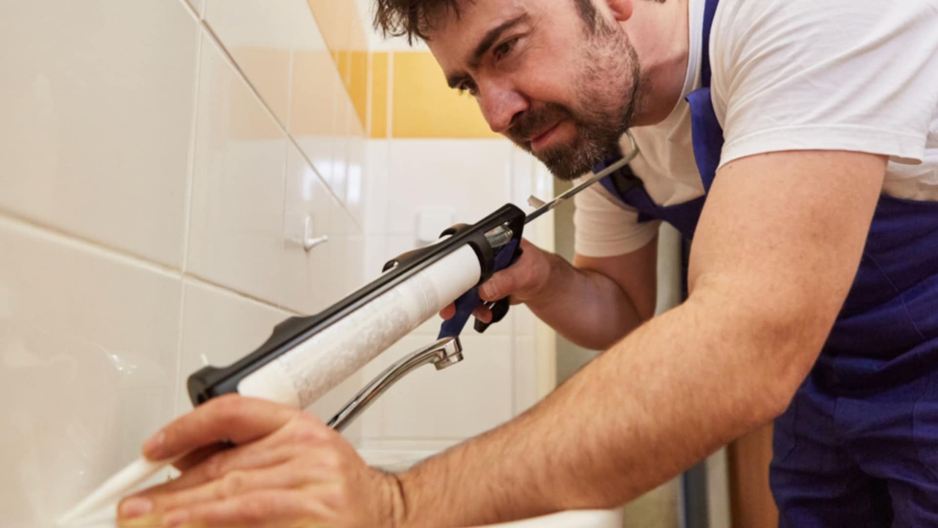 close up of person using caulking gun to seal bathroom joint