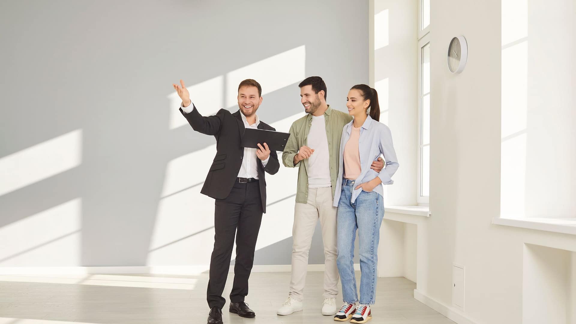 Real estate agent showing happy couple around bright empty room while touring a home