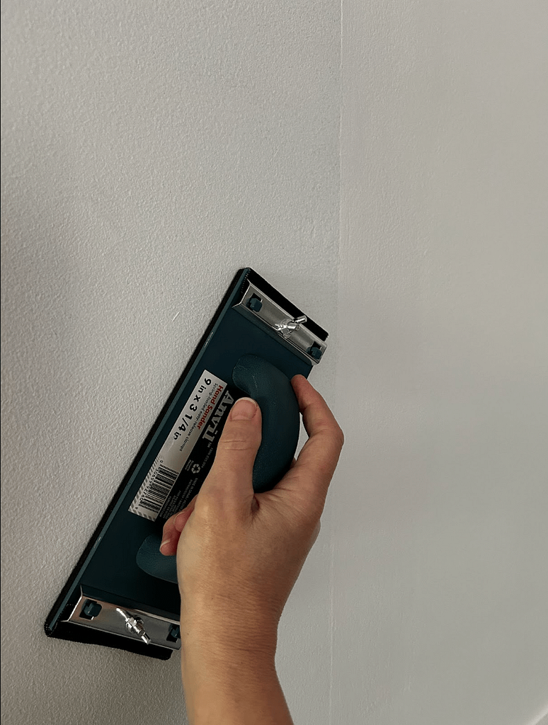 Hand sanding wall corner as part of preparing walls for painting
